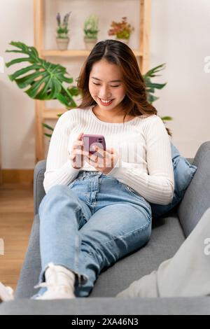 Donna che sorride al telefono mentre è seduta sul divano Foto Stock