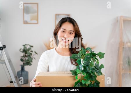 Donna sorridente tenendo in mano una pianta in vaso e una scatola di cartone Foto Stock