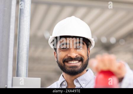 Un uomo sorridente con una barba che indossa un elmetto bianco premendo il pulsante rosso Foto Stock