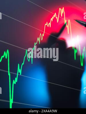 Una sagoma sfocata di una persona è visibile in primo piano con lo sfondo di un grafico del mercato azionario che mostra una linea di tendenza fluttuante in rosso e verde. Foto Stock