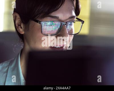 Un individuo attento che indossa occhiali con riflesso del codice del computer nelle lenti sta guardando con attenzione lo schermo di un computer. Foto Stock