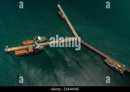 Veduta aerea di un molo con due navi attraccate su entrambi i lati, con una piccola struttura all'estremità e container sul molo. Foto Stock