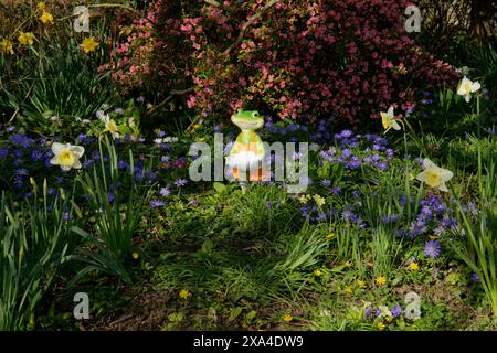 Una statuetta a forma di rana, in mezzo ai fiori del giardino, in primavera. Foto Stock