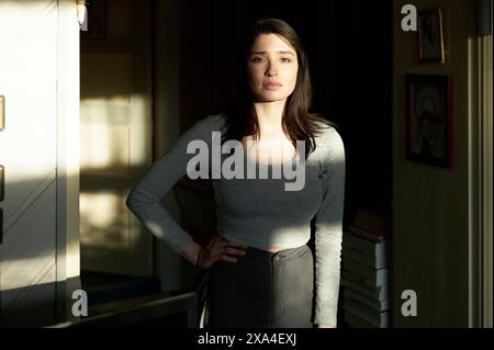 Una donna sta in una stanza illuminata dal sole, parzialmente gettata nell'ombra, con un'espressione calma sul suo volto. Foto Stock