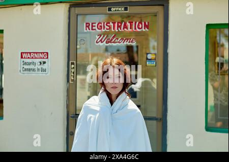 Una persona avvolta in una coperta bianca si trova di fronte a un edificio con un cartello che dice REGISTRAZIONE benvenuto. Foto Stock