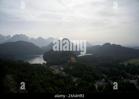 Una vista serena su una valle boscosa con un castello arroccato su una collina accanto a un lago, sotto un cielo nuvoloso al crepuscolo. Foto Stock