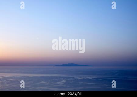 Una vista serena di un mare tranquillo al crepuscolo con un'isola sagomata in lontananza sotto un cielo in pendenza che passa dal rosa caldo al blu freddo. Foto Stock
