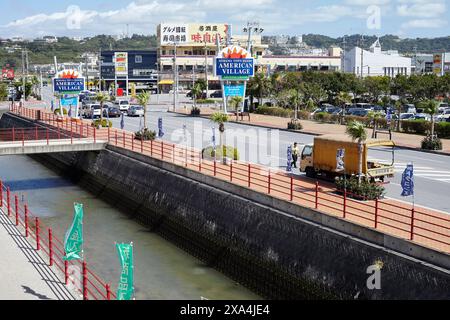 Si tratta di un'immagine all'aperto che mostra un canale con una ringhiera rossa accanto e un ponte in lontananza. Ci sono vari cartelli e striscioni, con IL VILLAGGIO AMERICANO visibile su un cartellone blu." Foto Stock