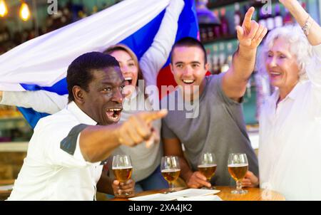 Allegri tifosi di calcio diversi con la bandiera della Russia trascorrere il tempo insieme con pinta di birra nel pub Foto Stock