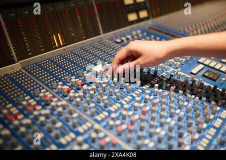 Un'immagine ravvicinata di cursori regolabili a mano su una console di missaggio audio professionale con contatori di livello colorati e varie manopole. Foto Stock