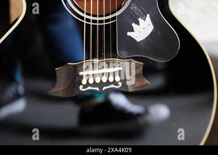 Questa è una foto ravvicinata di una chitarra acustica nera che mostra le corde, il buco del suono e il ponte, con un riflesso visibile sul corpo. Foto Stock