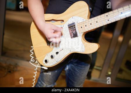 Primo piano di una persona che suona una chitarra elettrica con una selezione, focalizzata sulla chitarra e sulla mano con uno sfondo sfocato. Foto Stock