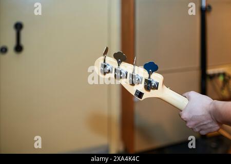 Uno scatto ravvicinato della mano di una persona che sintonizza i perni sulla testa di una chitarra basso su uno sfondo sfocato. Foto Stock