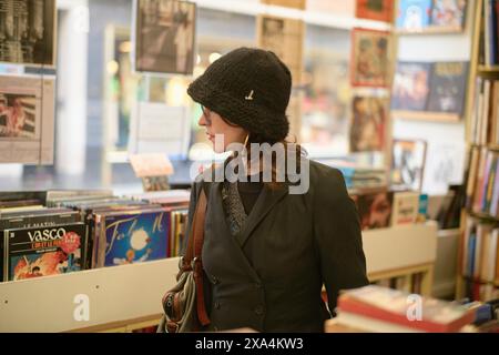 Una donna che indossa un cappello nero e un cappotto sta navigando in una libreria con un comportamento premuroso, la sua attenzione si è concentrata sui libri che le sono di fronte. Foto Stock