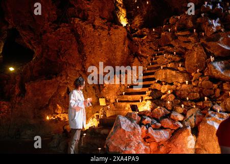 Una giovane donna si trova all'interno di una caverna poco illuminata con gradini illuminati che conducono verso l'alto e tengono in mano un blocco note. Foto Stock