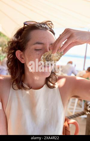 Una donna sta mangiando un'ostrica in un ristorante sul mare. Foto Stock