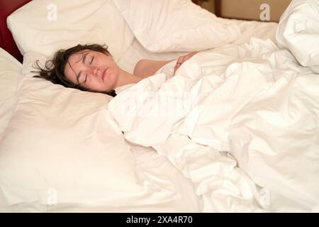 Una persona dorme tranquillamente in un letto ricoperto da un piumone bianco in un'accogliente camera da letto. Foto Stock