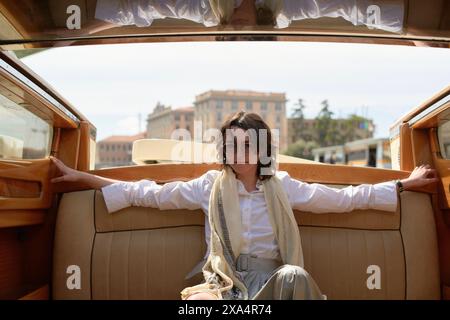 Giovane donna che si gode un lussuoso giro su un'auto d'epoca con sfondo cittadino. Foto Stock