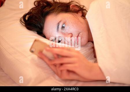 Giovane donna che usa uno smartphone a letto Foto Stock