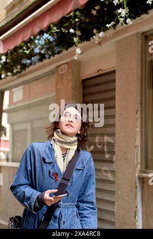 Giovane donna in giacca di denim che passeggiava per la città con una macchina fotografica. Foto Stock