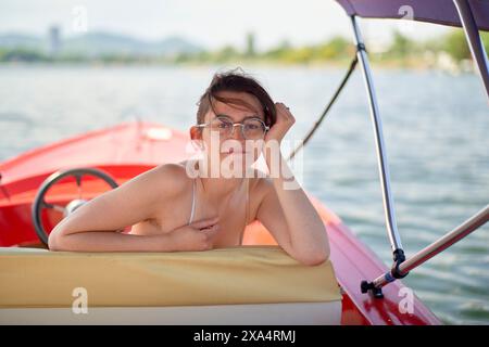 Donna sorridente che si gode una giornata di sole su un pedalò rosso Foto Stock