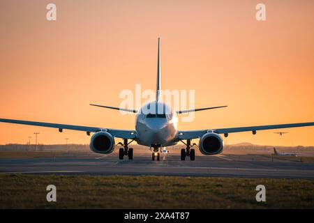 Traffico all'aeroporto al tramonto dorato. Vista frontale dell'aeroplano in rullaggio mentre altri decollano dalla pista. Foto Stock