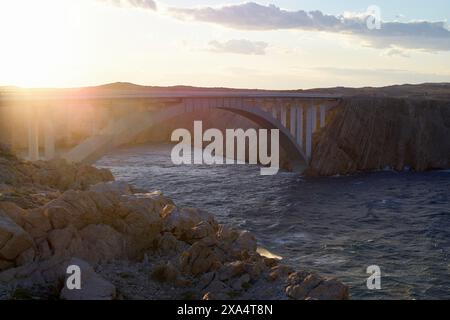 Il bagliore del tramonto illumina un ponte ad arco su un fiume tranquillo con terreno roccioso che lo circonda. Foto Stock