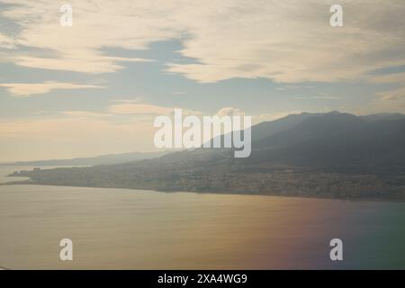 Paesaggio urbano costiero sullo sfondo di montagne sotto un cielo nebbioso al tramonto. Foto Stock