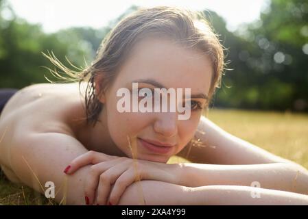 Primo piano di una donna sorridente sdraiata sull'erba, godendosi una giornata di sole. Foto Stock