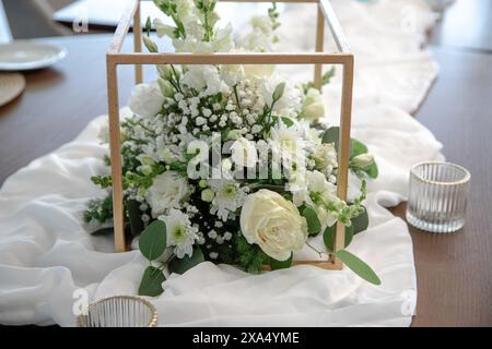 Un bellissimo centro floreale con rose bianche, margherite, ginecofila e vegetazione, elegantemente allestito in una cornice in legno Foto Stock