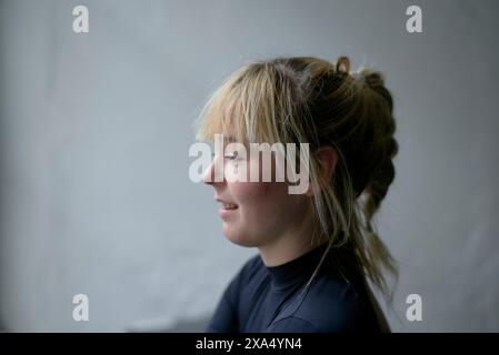Profilo laterale di una giovane donna sorridente con capelli biondi su sfondo grigio. Foto Stock