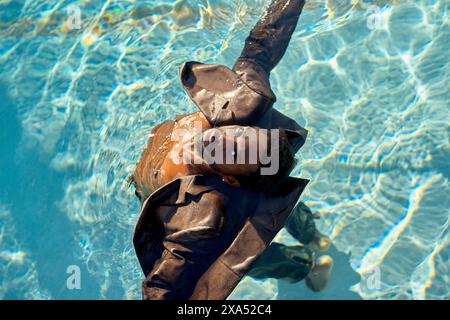 Uomo con una tuta che galleggia serenamente sulla schiena in una piscina azzurra sotto la luce del sole. Foto Stock