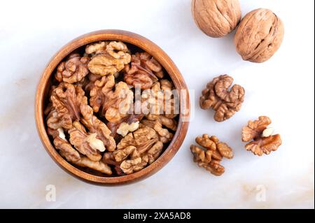 Le metà di noce si trovano in una ciotola di legno su un piatto di marmo. Chicchi sgusciati ed essiccati, semi maturi del comune albero di noce Juglans regia. Foto Stock