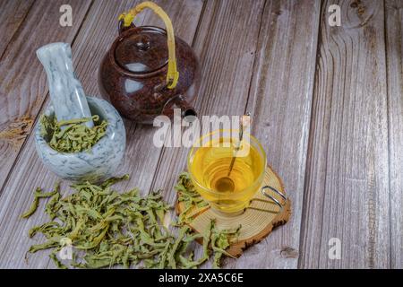 Un infuso di verbena al limone in una tazza di vetro con mortaio di marmo e pestello e una teiera in ceramica Foto Stock