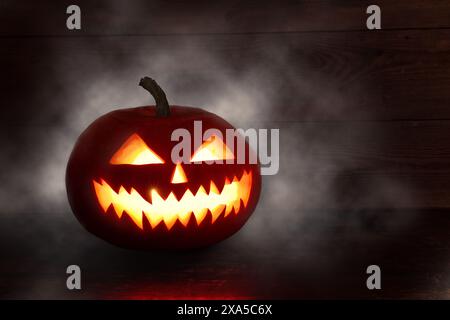 Spaventosa zucca di Halloween con gli occhi che brillano all'interno su sfondo scuro. Spaventosa zucca di Halloween, Jack o Lantern, con un volto malvagio e gli occhi su un legno Foto Stock