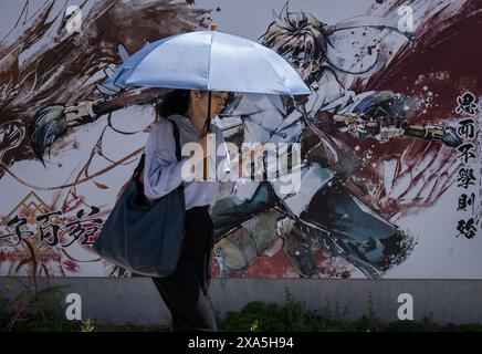 Una donna con un ombrello cammina accanto a un colorato muro di graffiti a Yokohama, in Giappone. Foto Stock