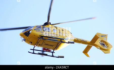 L'Air Ambulance che vola in Scozia, Regno Unito, contro il cielo azzurro Foto Stock