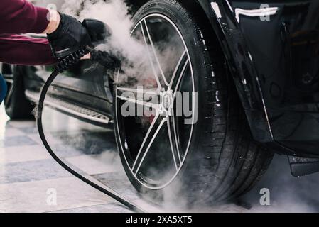 Primo piano di una persona che utilizza un tubo flessibile per pulire le ruote dell'auto Foto Stock