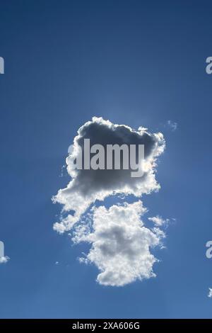 Il sole dietro una nuvola contro un cielo azzurro che emana luce da dietro Foto Stock