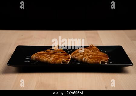 Un piatto di pancake condito con sciroppo su un piatto nero Foto Stock