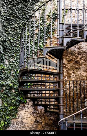 Un'antica scala a chiocciola in ferro con ringhiere ornate, adiacente ad un muro di mattoni Foto Stock