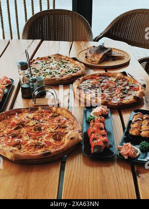 Un primo piano di varie pizze e sushi esposto su un tavolo in un ristorante all'aperto Foto Stock