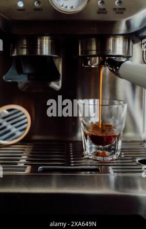 Una persona che versa caffè appena estratto da una macchina per il caffè in una tazza. Foto Stock