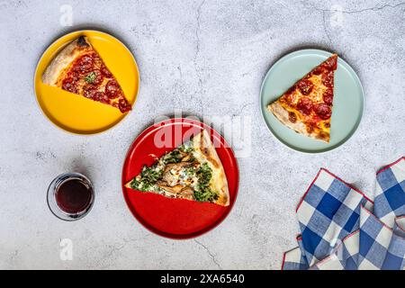 Una selezione di fette di pizza su piatti gialli e rossi con tovagliolo e vino rosso Foto Stock