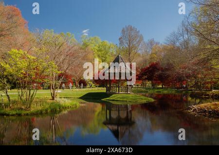 Gazebo con tetto a punta sulla riva erbosa di uno stagno in un parco Foto Stock