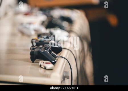 Una linea di controller di gioco disposti su un tavolo con i cavi collegati Foto Stock