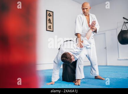 Due uomini si allenano in aikido con uno che applica la tecnica Hiji kime osae della chiusura articolare sono vestiti con kimono e hakama, practici delle arti marziali tradizionali Foto Stock