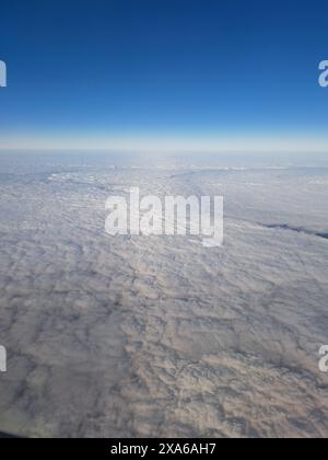 Un aereo che vola attraverso nuvole soffici contro un cielo blu limpido Foto Stock