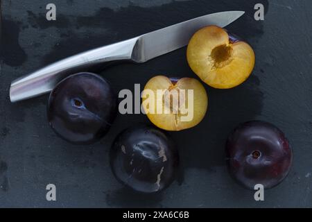 foto ravvicinata da tavolo di mezze fette di prugne blu scuro con coltello in acciaio su sfondo scuro, fotografia di natura morta con cibo basso Foto Stock