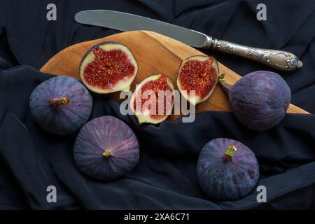 foto da tavolo di un gruppo di frutti di fico tagliati e interi con coltello vintage e tagliere in legno su sfondo scuro Foto Stock